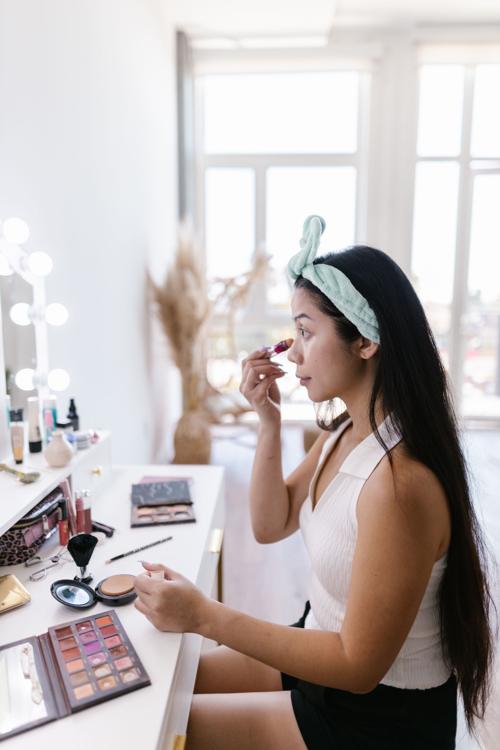 Young woman applying makeup at an illuminated vanity table