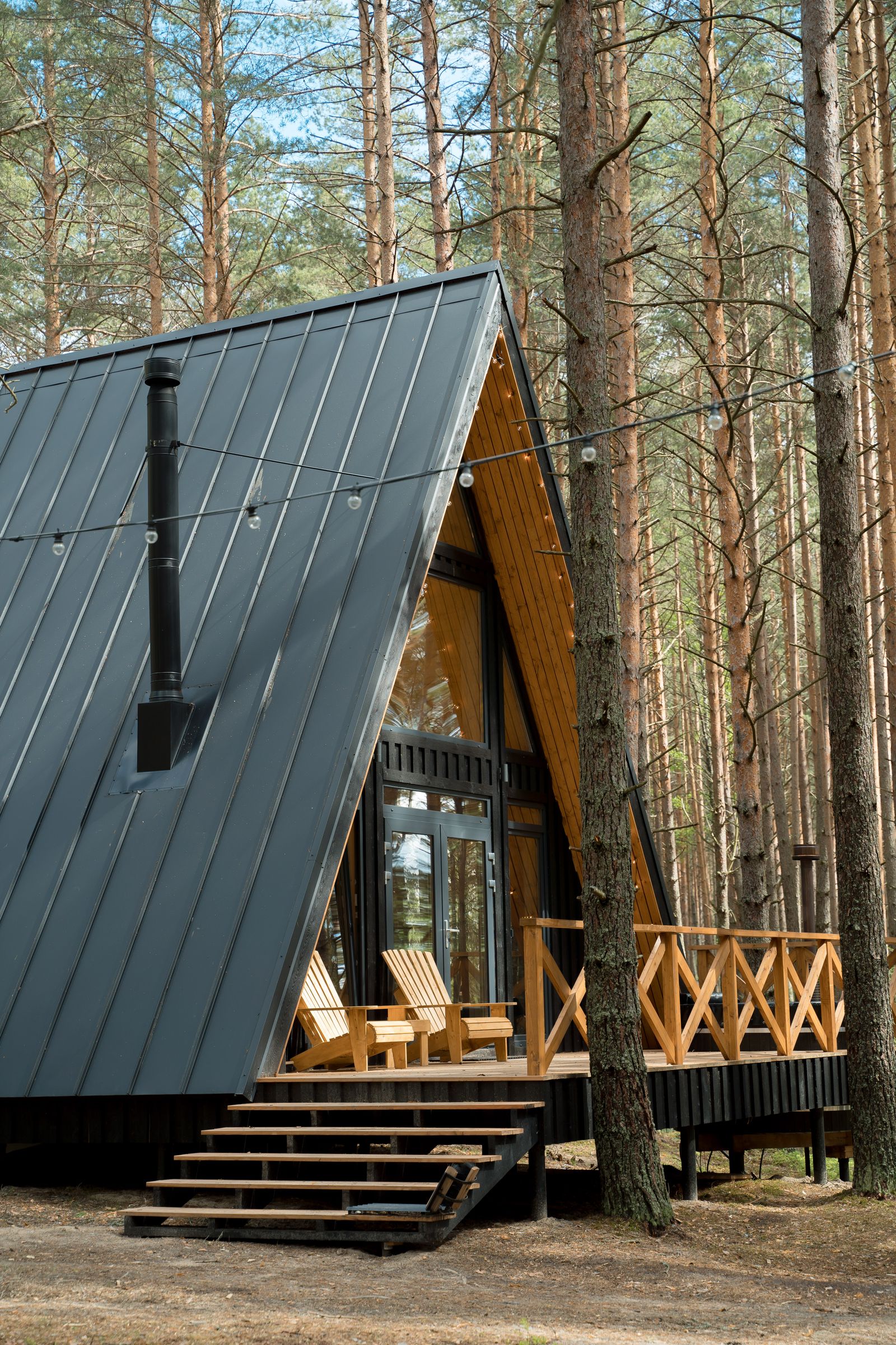 Modern cabin with a wooden porch surrounded by tall trees