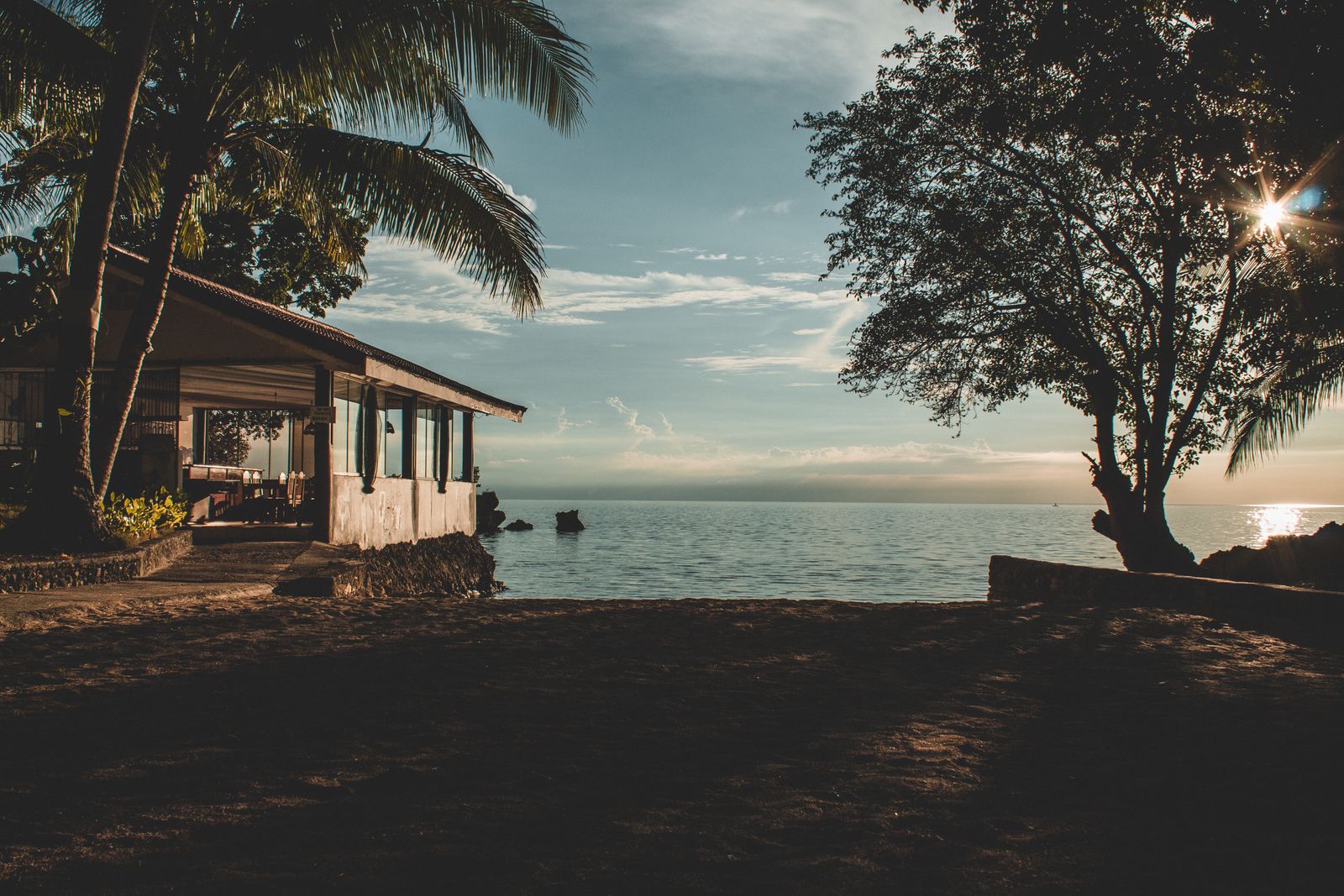 House standing near a beach with sand and sea behind it